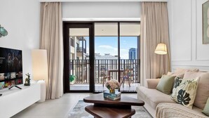 Ein modernes Wohnzimmer mit einer Couch, einem Couchtisch und einem Fernseher. Ein Balkon bietet Blick auf Gebäude.