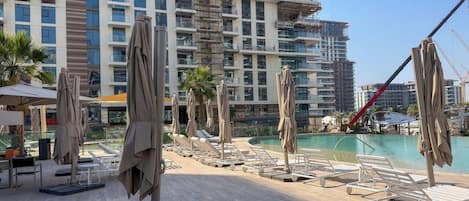 A poolside area with lounge chairs and umbrellas, a clear sky, and a building under construction in the background.