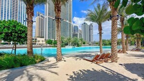 A beach area with palm trees, lounge chairs, and a pool. - Beachside 3BR with Pool Views & Lagoon Access (Dubai)