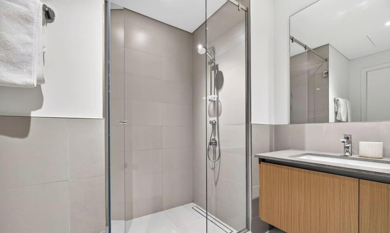 A modern bathroom with a glass shower enclosure, a sink with a mirror, and wooden cabinetry.