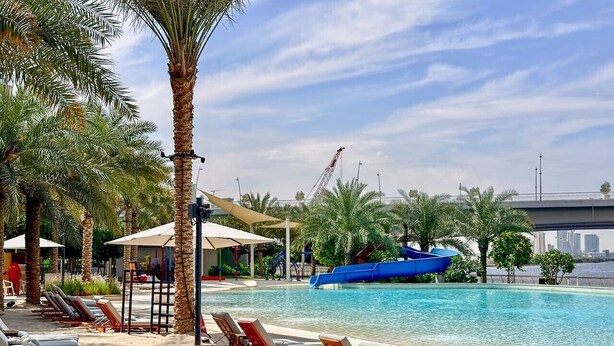 A poolside area with lounge chairs, palm trees, and a blue slide. - Beachside 3BR with Pool Views & Lagoon Access (Dubai)