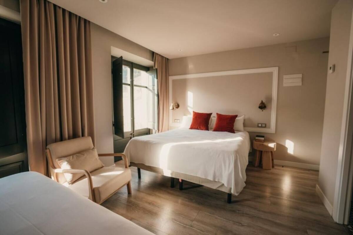 A hotel room with a bed, a chair, a nightstand, and a window.