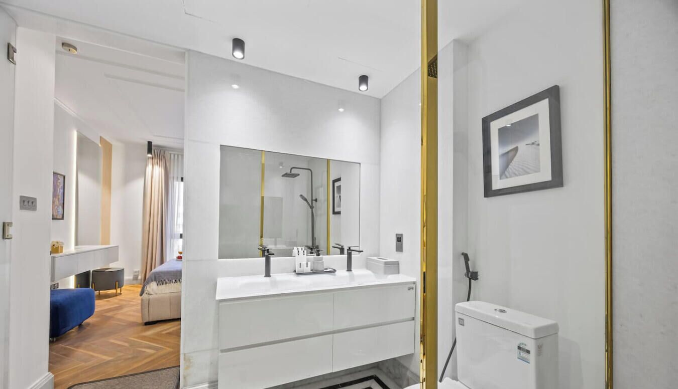A modern bathroom with a large mirror, two sinks, and a toilet.