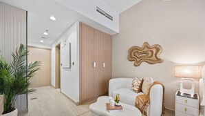 Quarto de hotel moderno com sofá, mesa de cabeceira, luminária e uma grande planta em vaso.