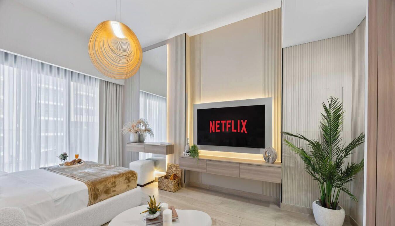 A modern living room with a large flat-screen TV displaying 'NETFLIX,' a sofa, a coffee table, and a potted plant.