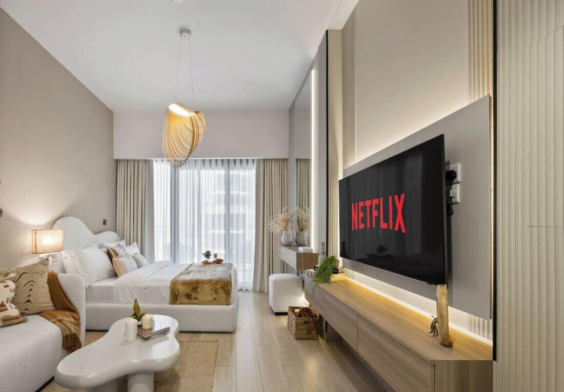 A modern hotel room with a large flat-screen TV, a sofa, a coffee table, and a fireplace.