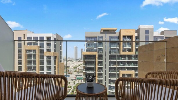 Uma varanda com móveis de vime, uma pequena mesa e vista para edifícios modernos.