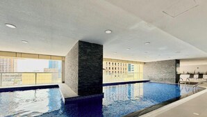 A modern indoor swimming pool with a city view, a stone pillar, and a seating area. - Mediterranean Prestige 2BR | Sulafa Tower, Marina (Dubai)