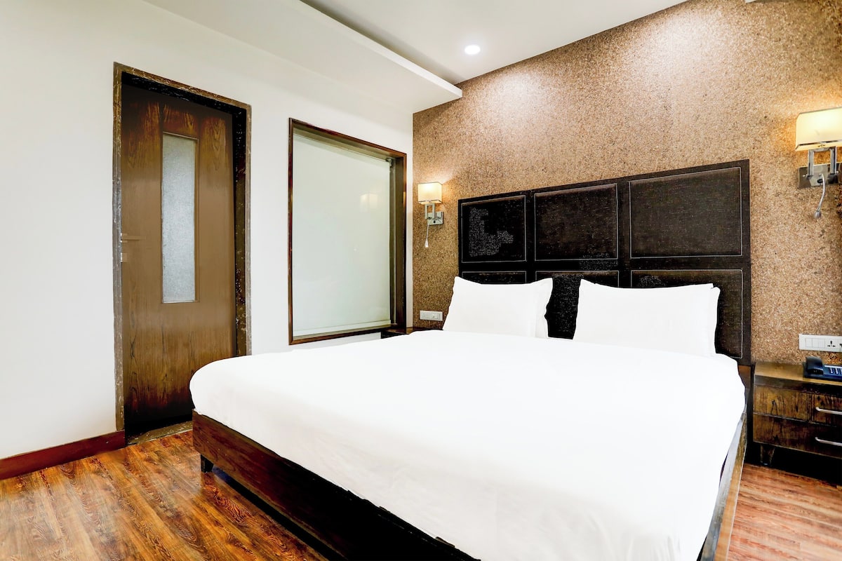 Ein Hotelzimmer mit einem großen Bett, Holzboden, einem dunklen Kopfteil und einer Wandleuchte.