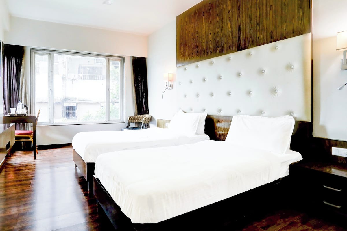 Ein Hotelzimmer mit zwei Betten, einem Schreibtisch, einem Stuhl, einem Fenster und einer Wand mit Holzverkleidung.