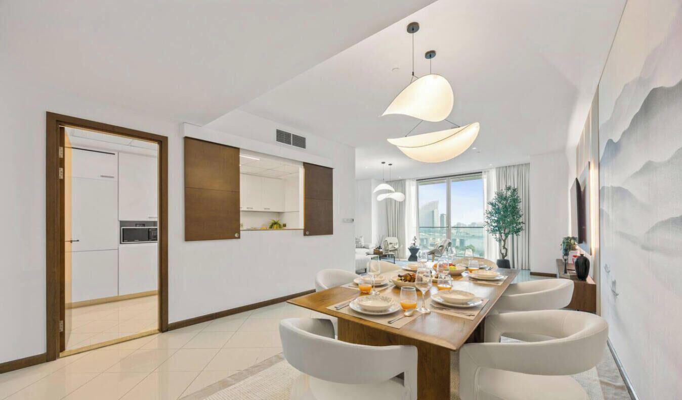 A modern dining area with a long table, white chairs, and pendant lighting.