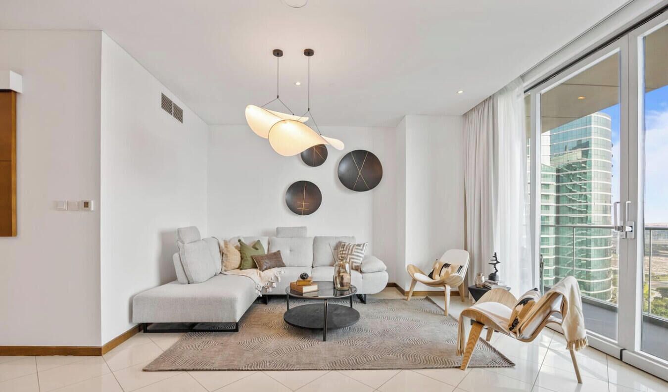 A modern living room with a sofa, coffee table, and chairs, a large window with a view, and a ceiling light fixture.