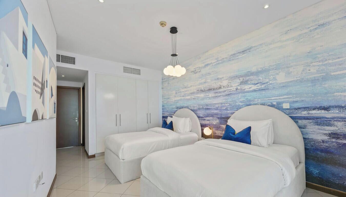 Een hotelkamer met twee bedden, een groot abstract kunstwerk aan de muur, een witte kledingkast en een plafondlamp.