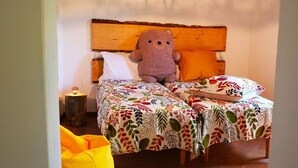 Sänky, jossa on puinen pääty, kaksi tyynyä, pehmolelu ja kukkakuviollinen päiväpeite.