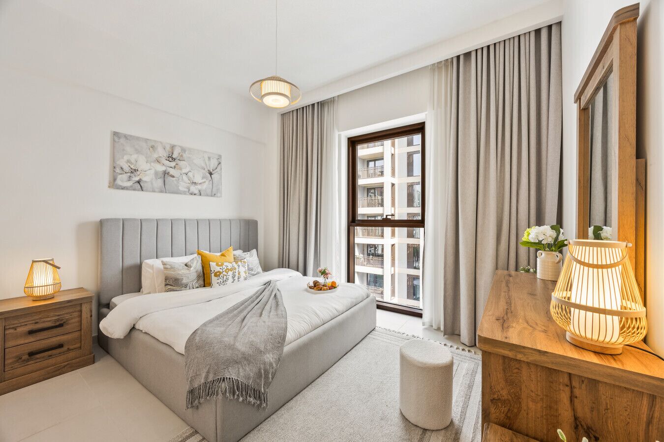 Un dormitorio moderno con cama, mesitas de noche, cómoda, ventana con cortinas y lámpara colgante.