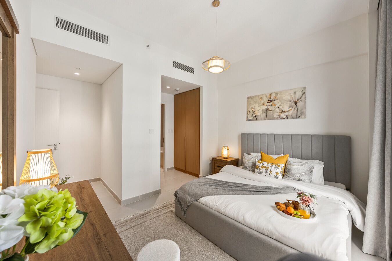 A modern hotel room with a large bed, bedside table, lamp, and a painting on the wall.