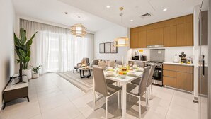 Eine moderne Küche mit Holzschränken, ein Essbereich mit Tisch für vier Personen und ein Wohnzimmer mit Sofa und großen Fenstern.