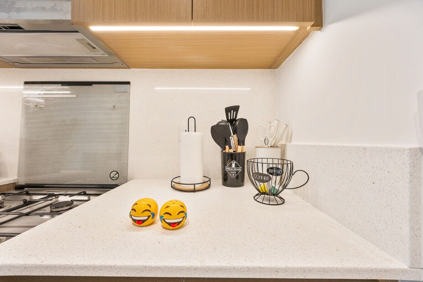 Ett kök med en gasspis, en hållare för hushållspapper, en kaffemaskin och en förvaringskorg för köksredskap.