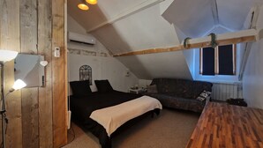 Une chambre de style « loft », avec un plafond en pente, un lit, un canapé, une table en bois et une fenêtre donnant sur un paysage agréable.