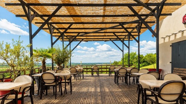 Une terrasse extérieure avec des tables et des chaises, une pergola et une vue sur la campagne.
