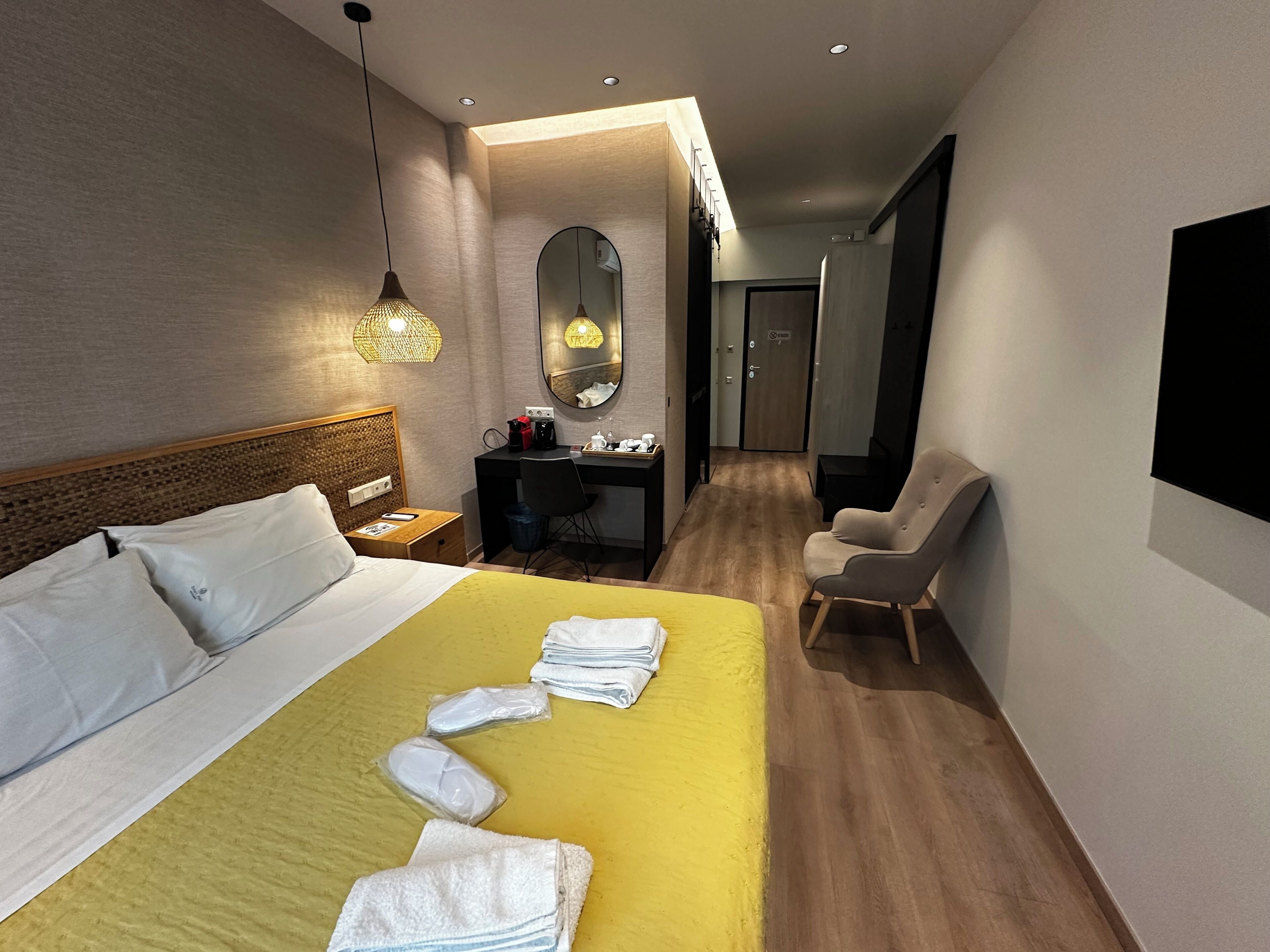 A hotel room with a bed, a desk, a chair, a mirror, and a TV.