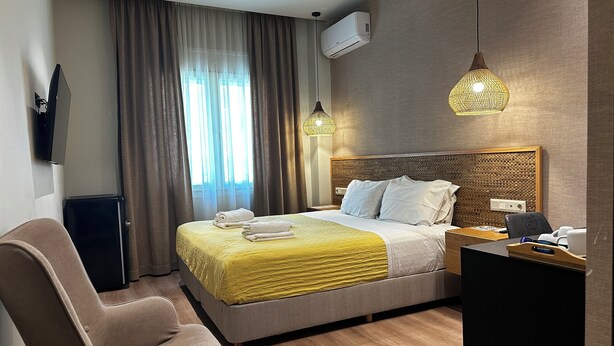 A hotel room with a bed, a desk, a chair, an air conditioner, and a window with curtains. - Syntagma Divine Guestrooms (Athens)