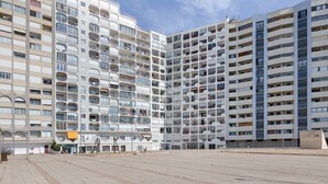 Un edificio moderno de gran altura, con múltiples balcones y una amplia plaza en su fachada.