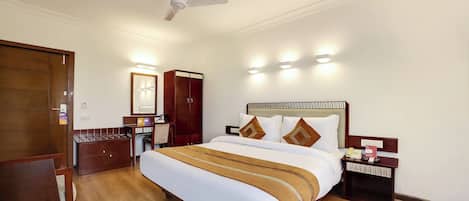 Habitación de hotel con cama, mesita de noche, armario, escritorio y ventilador de techo.