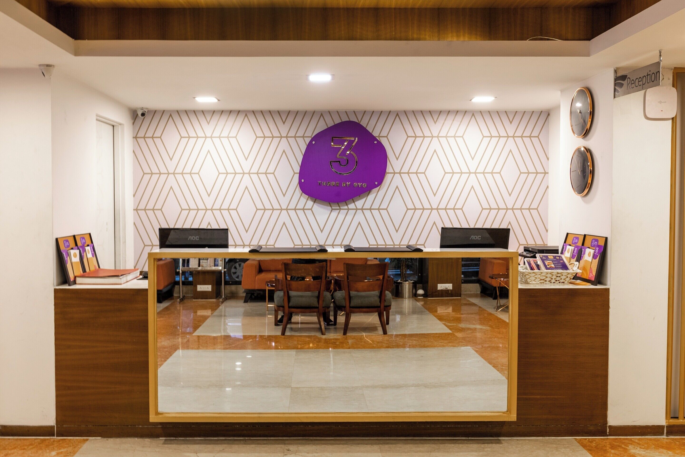 A reception desk with a geometric patterned wall, a reception sign, and a reception area with chairs and a counter.