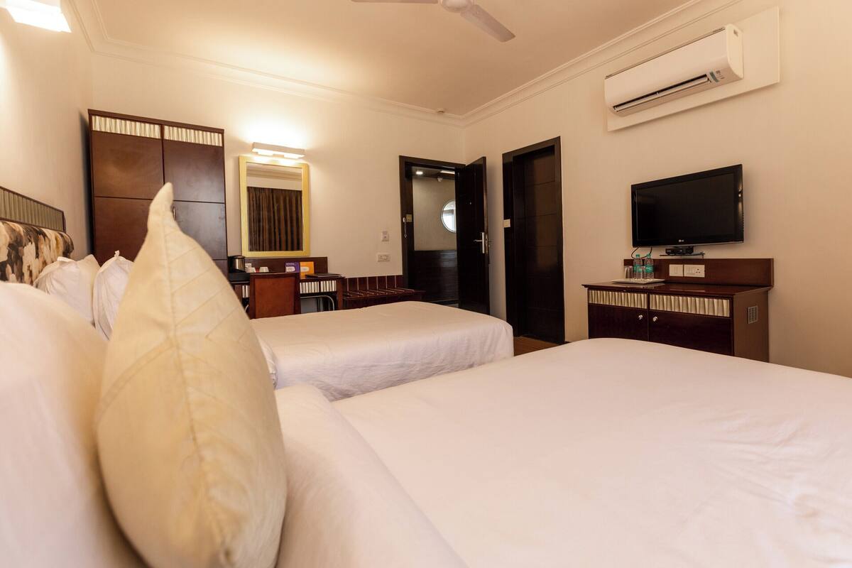 Una habitación de hotel con dos camas, televisión, aire acondicionado, espejo y armario.