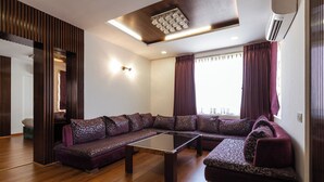 Ein modernes Wohnzimmer mit Ecksofa, Glastisch, Holzboden und einer Deckenleuchte.