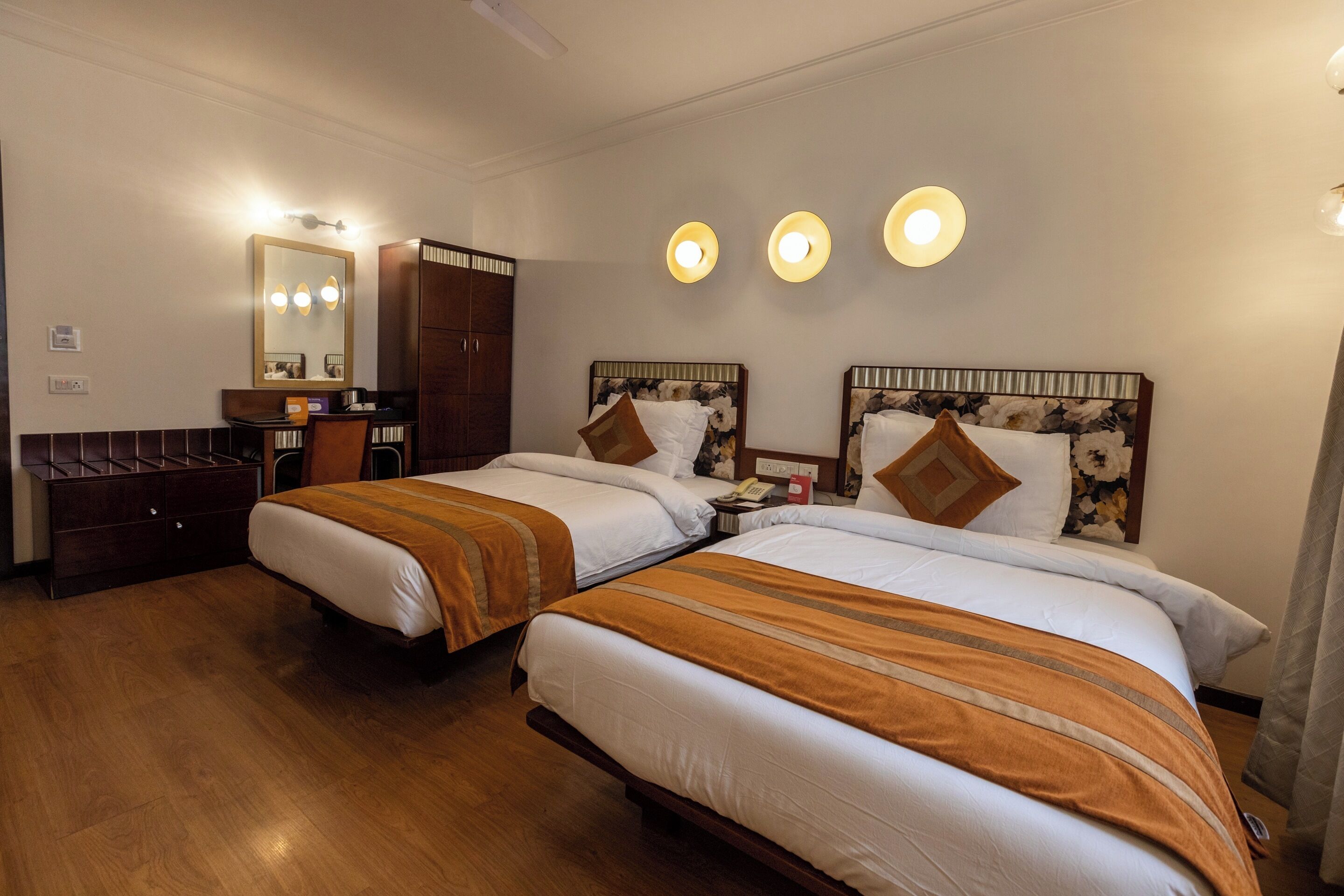 Ein Hotelzimmer mit zwei Betten, einem Holzschrank, einem Spiegel und drei Wandleuchten.