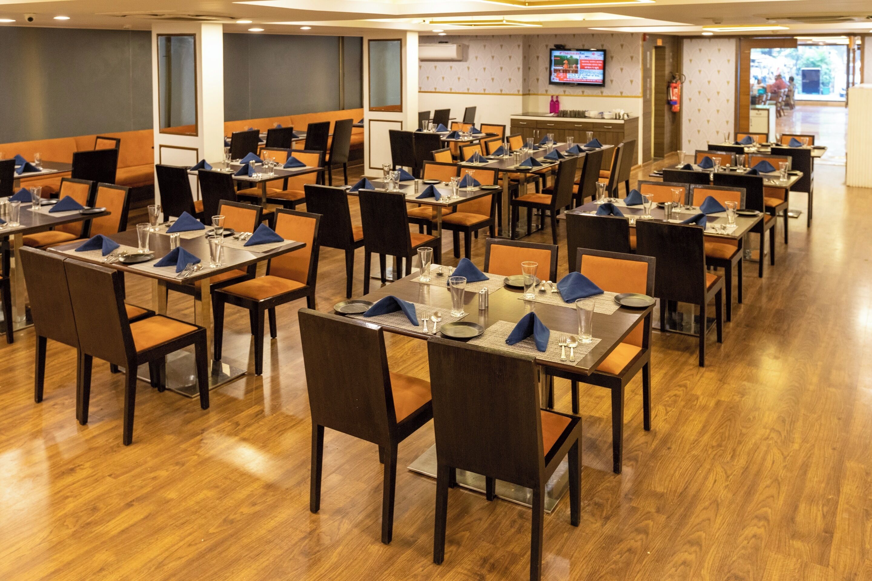 A restaurant with multiple tables and chairs, a television screen, and a fire extinguisher on the wall.