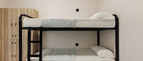 Una cama litera con escalera, un armario de madera y una pared blanca.