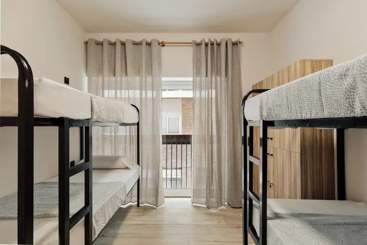 A dormitory room with bunk beds, a balcony, and a wooden wardrobe.