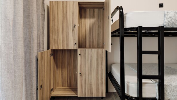 Una cama litera con un almacenaje de madera debajo, un escritorio plegable y una pared de color claro.