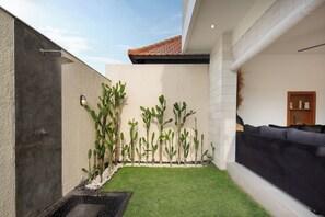 Un espace extérieur moderne avec une douche en béton, une pelouse artificielle verte et un canapé noir.