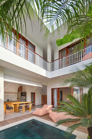 Un espace piscine intérieur à plusieurs niveaux, doté d’une terrasse en bois, de sièges et offrant une vue sur le ciel.