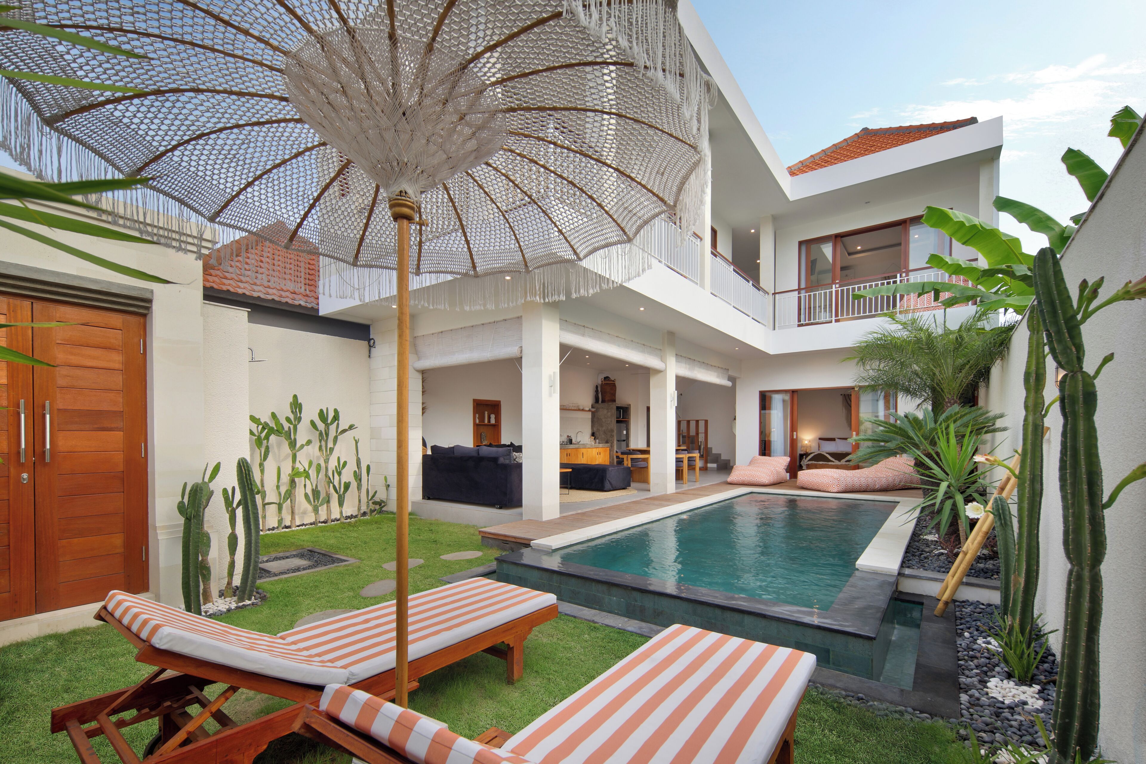 Une maison moderne dotée d’une piscine, d’un espace salon extérieur et d’un grand parasol.