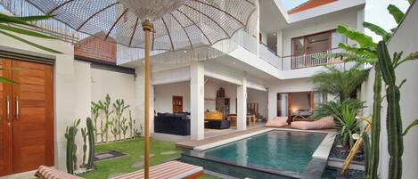 A modern house with a swimming pool, outdoor seating, and a large umbrella.