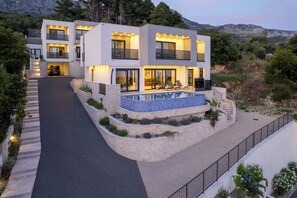 Ein modernes, zweistöckiges Haus mit Swimmingpool, Auffahrt und Blick auf die umliegende Landschaft.