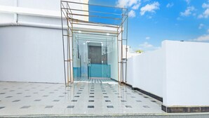 A modern building with a glass entrance, a metal frame structure, and a tiled floor. - Super Deluxe FTL Kompally Property (Hyderabad)