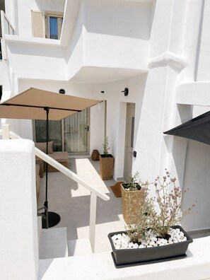 A white building with a covered outdoor seating area, a staircase, and potted plants. - Brand-New Boutique Apartment with Private Courtyard in Naxos Town (39XH+Q9C Naxos)