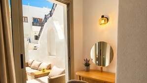Una habitación con puerta de cristal corredera que da a un balcón, un espejo redondo, un escritorio de madera y una silla acolchada.