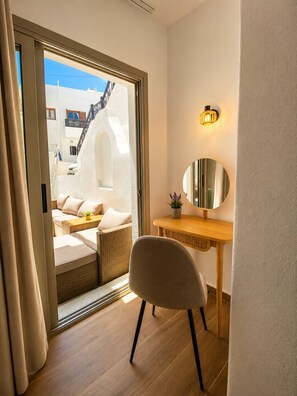A room with a sliding glass door leading to a balcony, a round mirror, a wooden desk, and a cushioned chair. - Brand-New Boutique Apartment with Private Courtyard in Naxos Town (39XH+Q9C Naxos)