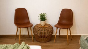 Una habitación con dos sillones de cuero marrón, una mesita redonda de fibras naturales con una planta, y una manta verde sobre el suelo.