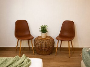 A room with two brown leather chairs, a round woven side table with a plant, and a green blanket on the floor. - Brand-New Boutique Apartment with Private Courtyard in Naxos Town (39XH+Q9C Naxos)