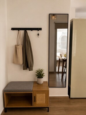 A room with a bench, a potted plant, a coat rack with keys, and a mirror reflecting a dining area. - Brand-New Boutique Apartment with Private Courtyard in Naxos Town (39XH+Q9C Naxos)