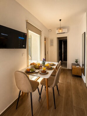 A modern dining area with a flat-screen TV, breakfast buffet, and a hallway leading to a bathroom. - Brand-New Boutique Apartment with Private Courtyard in Naxos Town (39XH+Q9C Naxos)