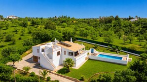 Eine moderne Villa mit Swimmingpool, umgeben von üppiger Vegetation und wolkenlosem, blauem Himmel.